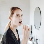 a woman washing her face with the leftover toothbrush water